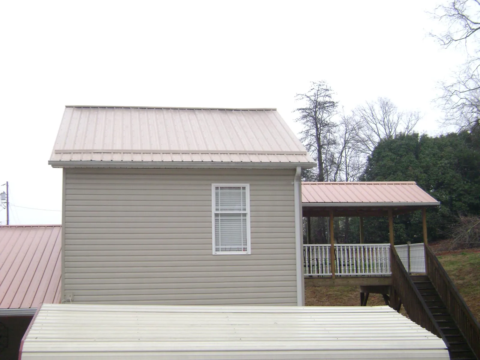 Tan metal roofs on a two story addition and attached porch, from a Roof Replacement job in Gilman